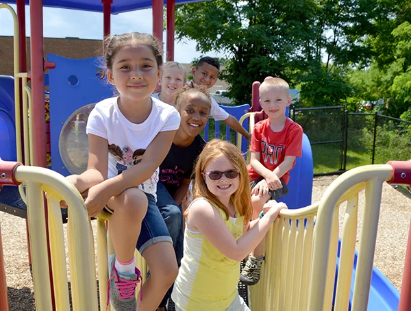The Merit School - Mission and Core Values - group of children smiling together on playground equipment
