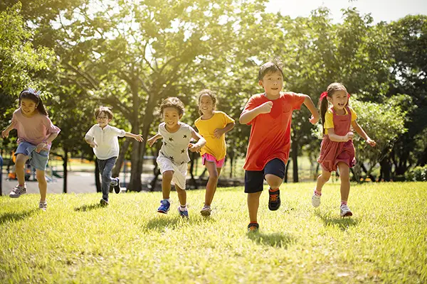 Summer Camp - children having fun running in field next to playground