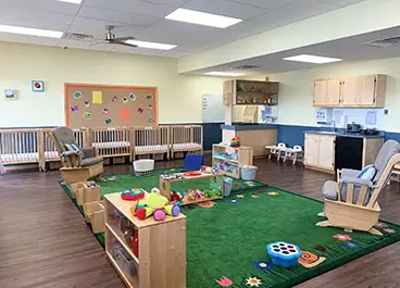 Merit School Infant Room - clean, bright, safe room with organized toys and learning materials, nursery rocking chairs, and cribs
