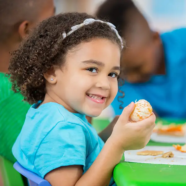 Preschool daycare childcare - smiling child sitting at table eating a peeled orange